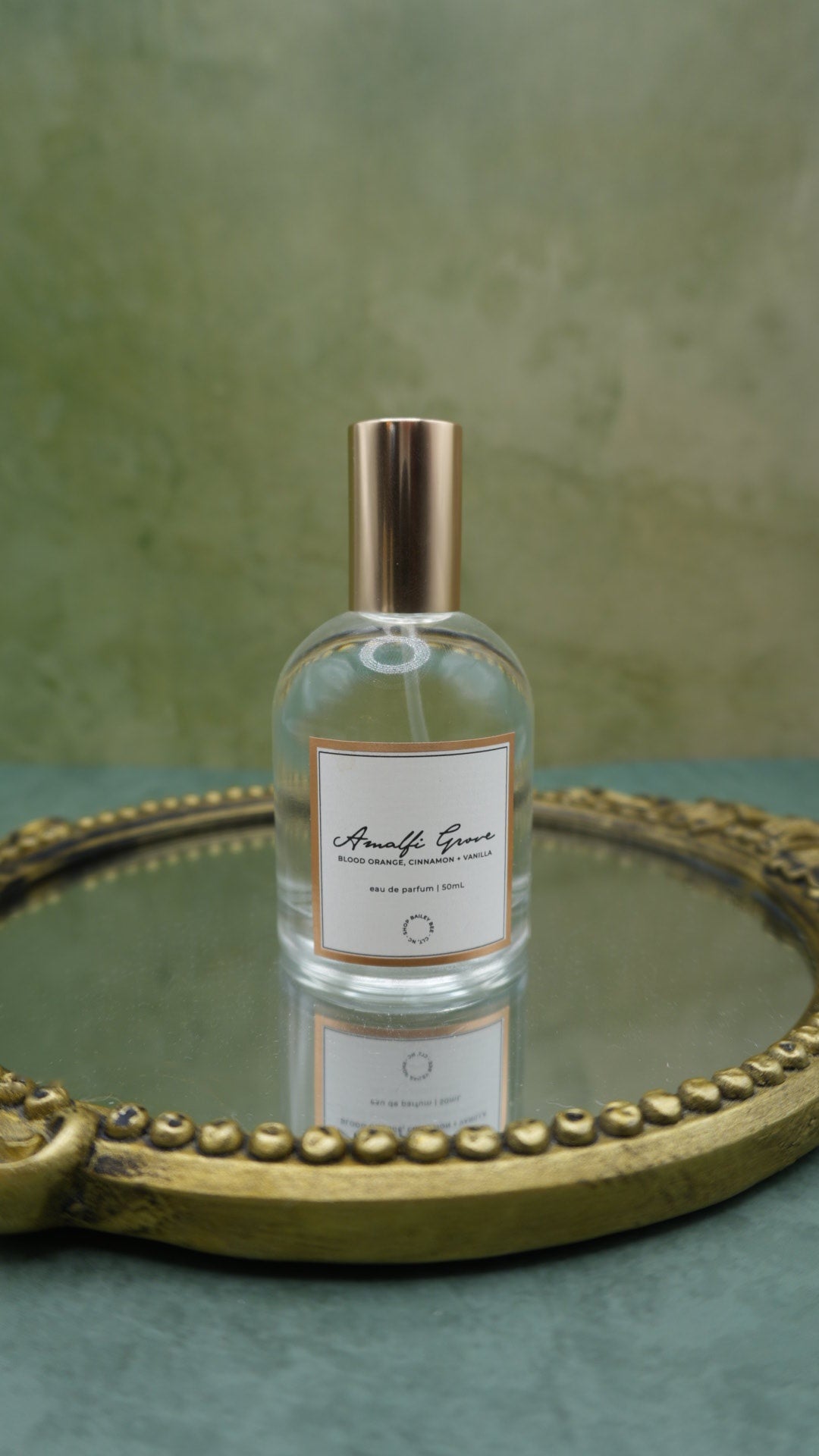 Bailey Bee Amalfi Grove Eau de Parfum 50ml bottle with gold cap on an antique gold mirrored tray, notes of blood orange, cinnamon and vanilla
